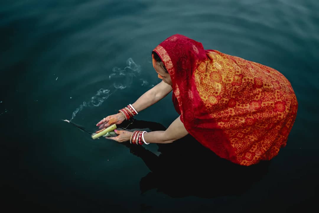 A woman in traditional attire performs Chhath Puja on a water body.