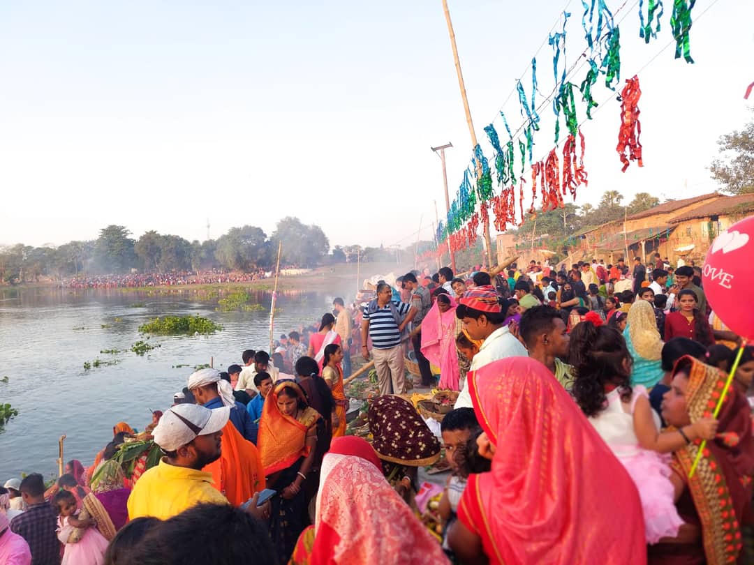 Crowd celebrating a traditional festival by the lake in Birpur, India with colorful attire and decorations.