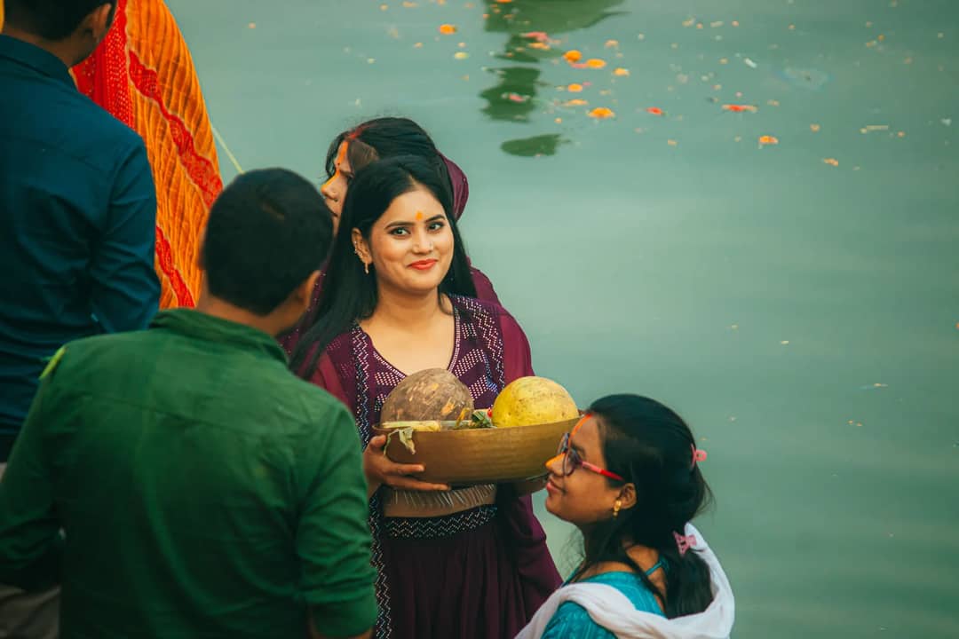 Women celebrating a traditional Hindu festival in Bihar, India with offerings by a river.