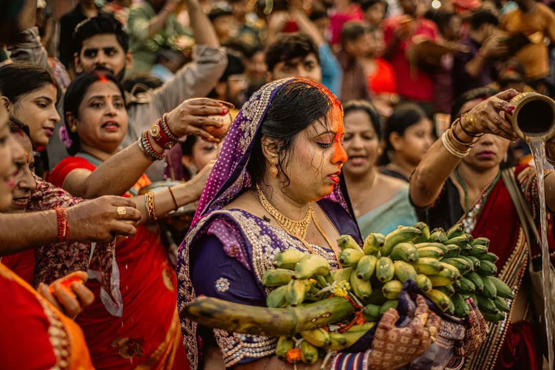 Colorful Chhath Puja ritual with women in traditional attire holding offerings in a vibrant crowd.