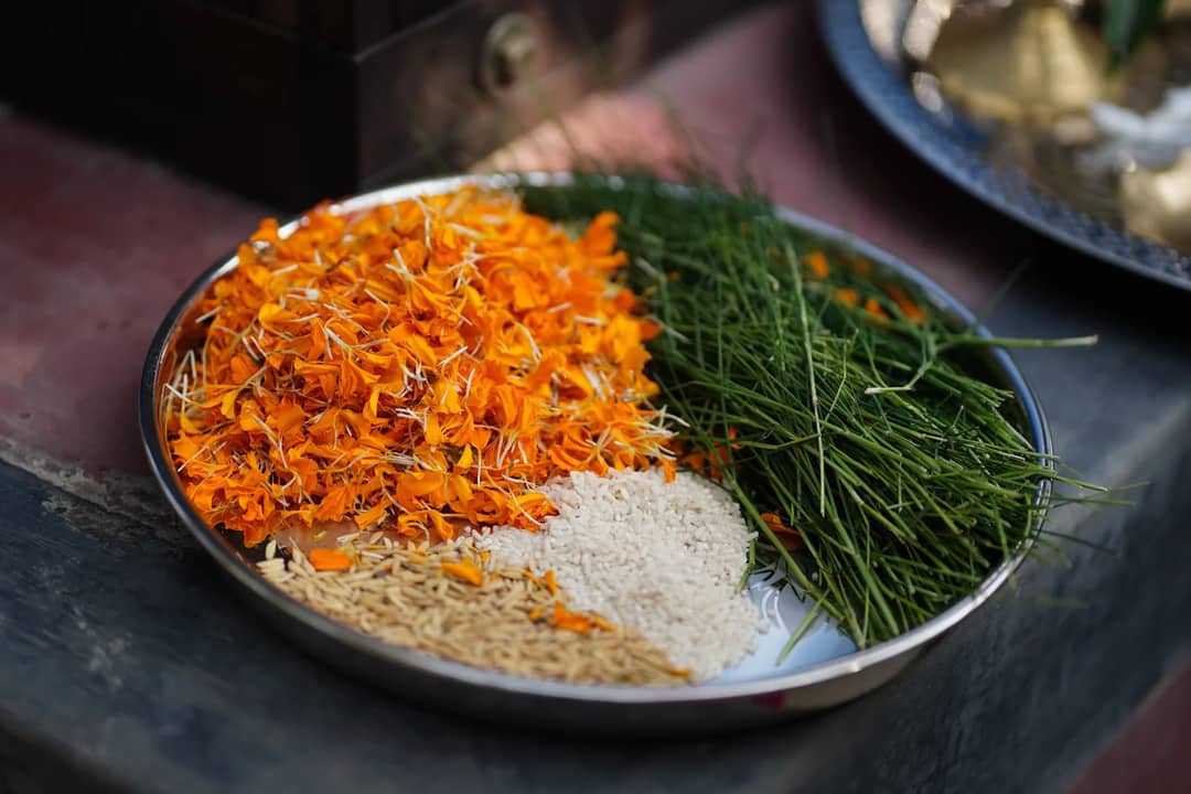 Metal plate with marigold petals, rice grains, and grass used in traditional Indian rituals.