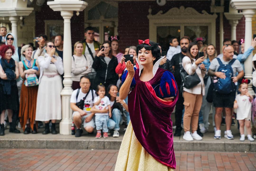 Snow White entertains a crowd at Disneyland Paris with joyful gestures.