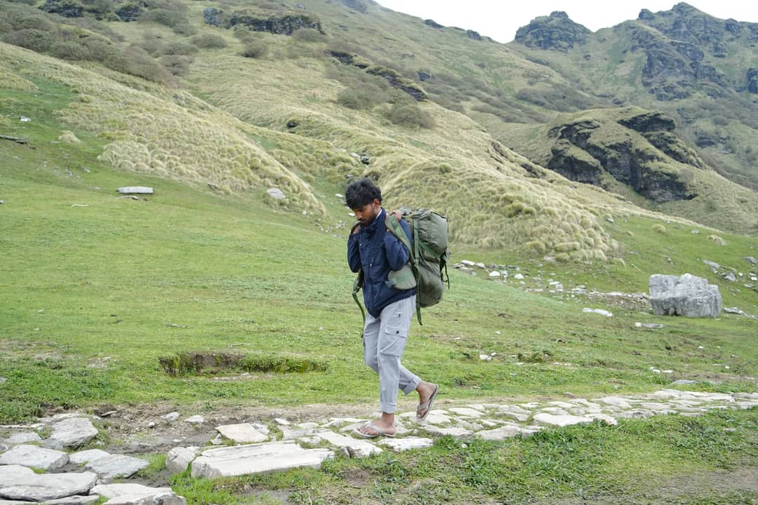 Man trekking through lush green hills in Gopeshwar, India with a large backpack, showcasing adventure and exploration.