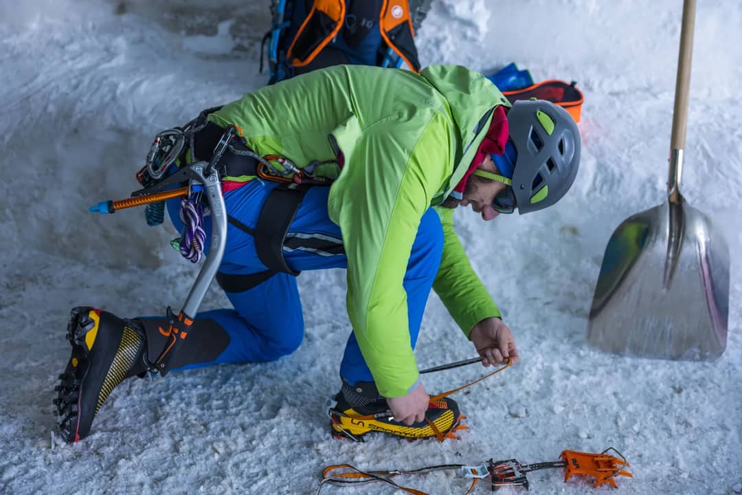 Climber in Chamonix adjusting crampons in an ice cave, ready for snowy adventure.