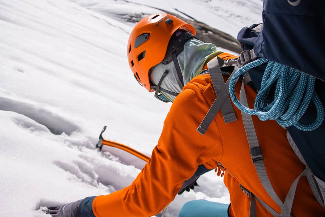A climber in bright orange gear traverses snowy mountain terrain during a winter ascent.