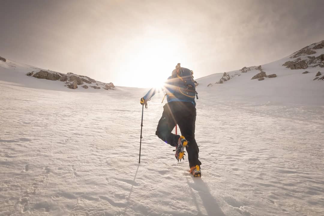 A climber with a backpack ascends a snowy mountain in Abruzzo, Italy, during sunrise.
