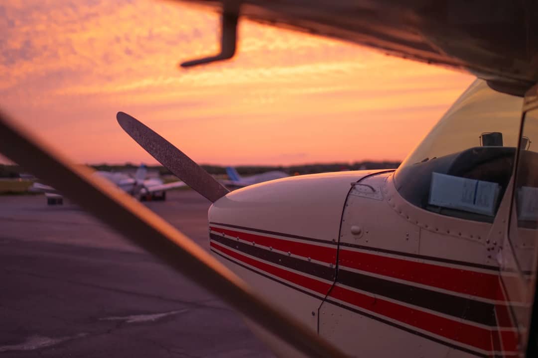 Close-up of a small propeller plane on the tarmac against a vibrant sunset sky, emphasizing aviation beauty.