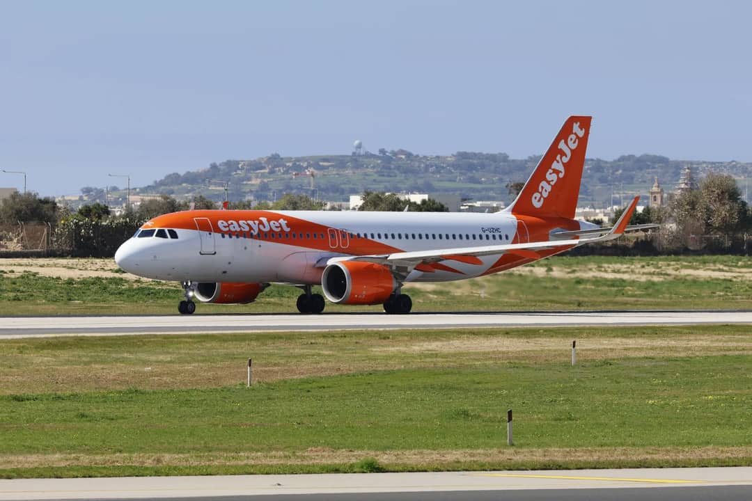 An EasyJet airplane taxiing on the runway at an airport with a scenic background.