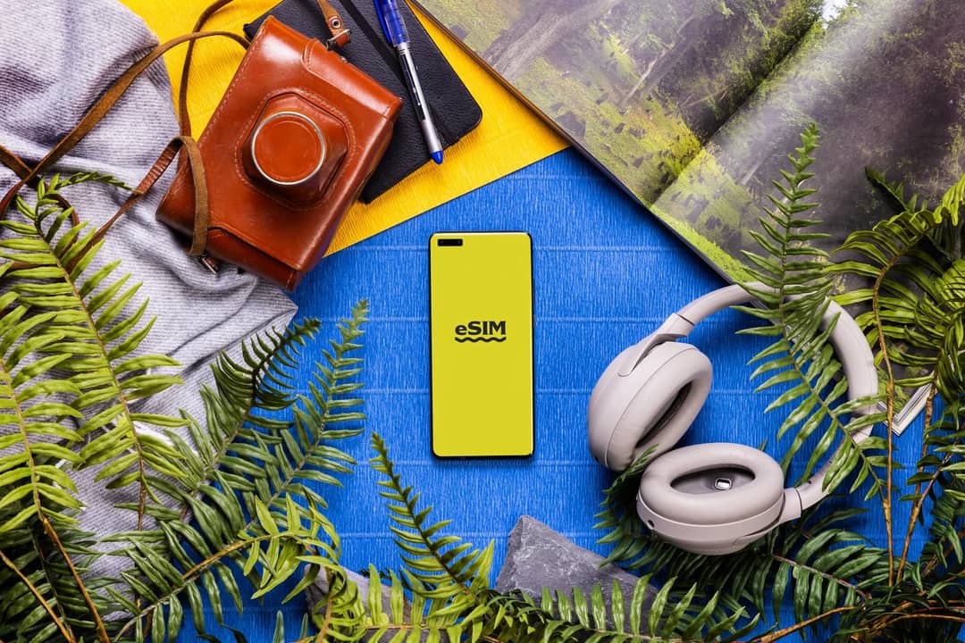 Flat lay of technology and travel essentials with a smartphone featuring eSIM on a colorful background.