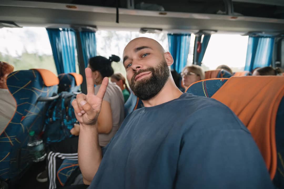 A man giving a peace sign while sitting in a bus with other passengers.