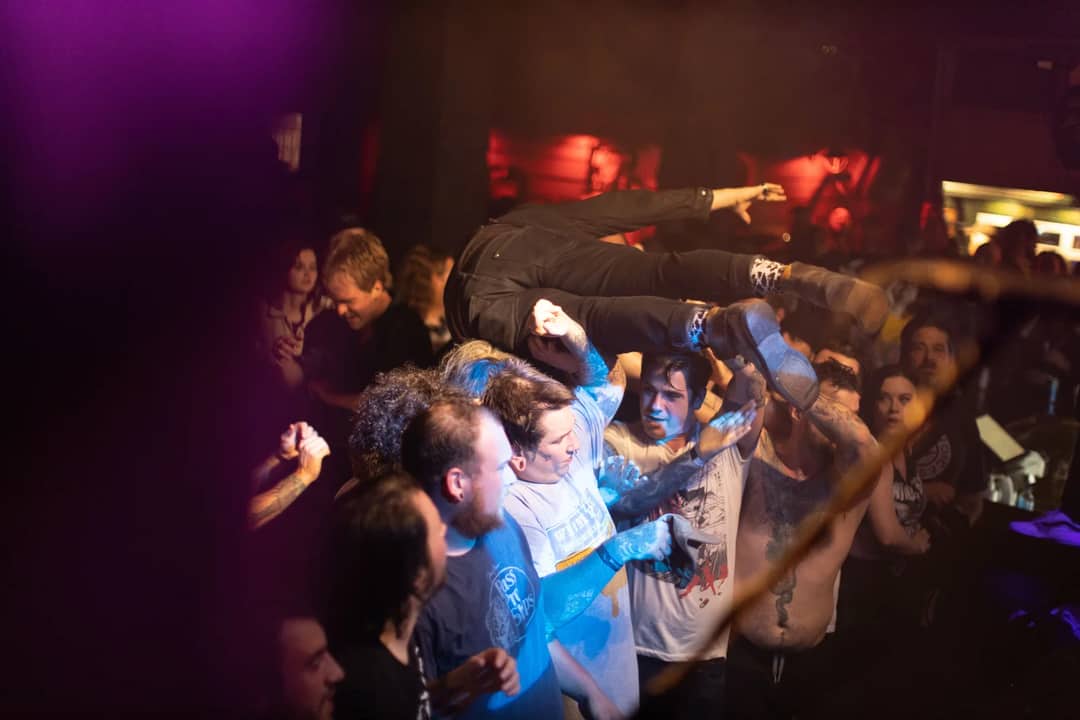 Dynamic scene of crowd surfing and celebration at a live music concert with enthusiastic audience.
