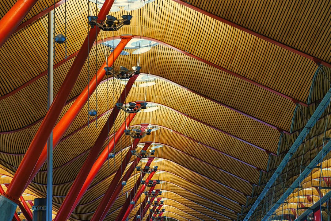 Intricate ceiling design of Madrid Barajas Airport with red poles and geometric patterns.