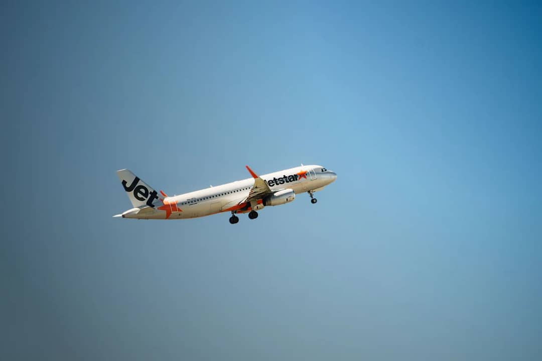 Jetstar airplane flying mid-air with clear blue sky backdrop