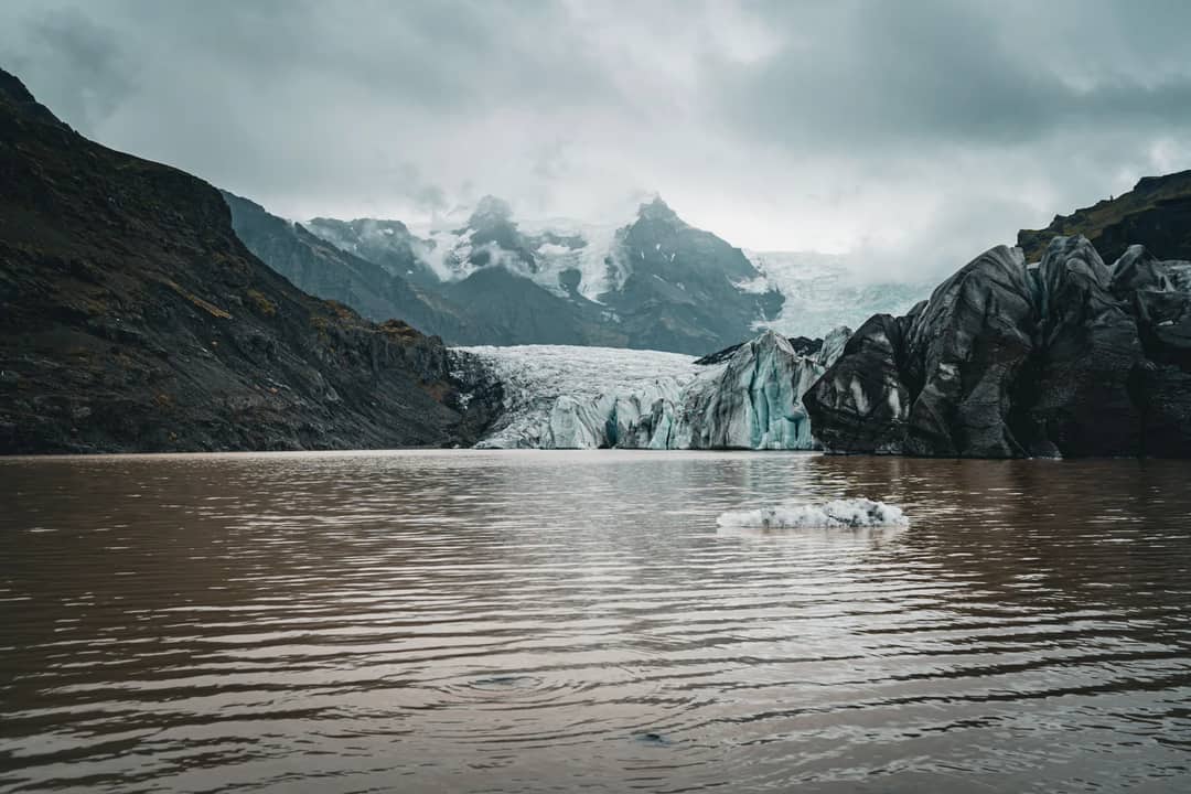 A breathtaking view of a glacier meeting a serene lake with mountains in Iceland.