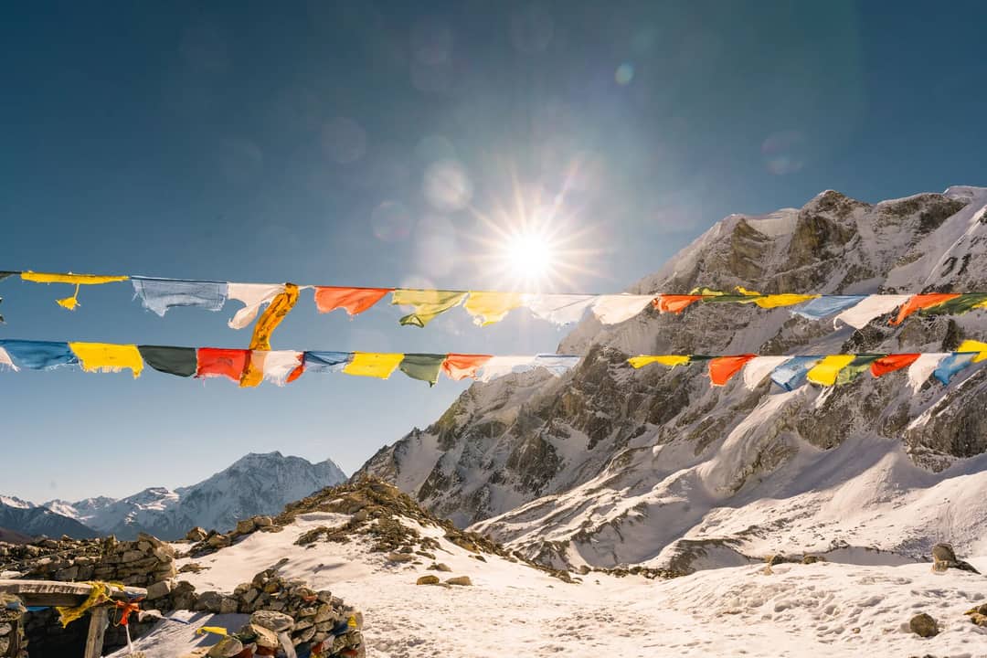 Colorful prayer flags against the stunning Himalayan mountains under a bright sun.