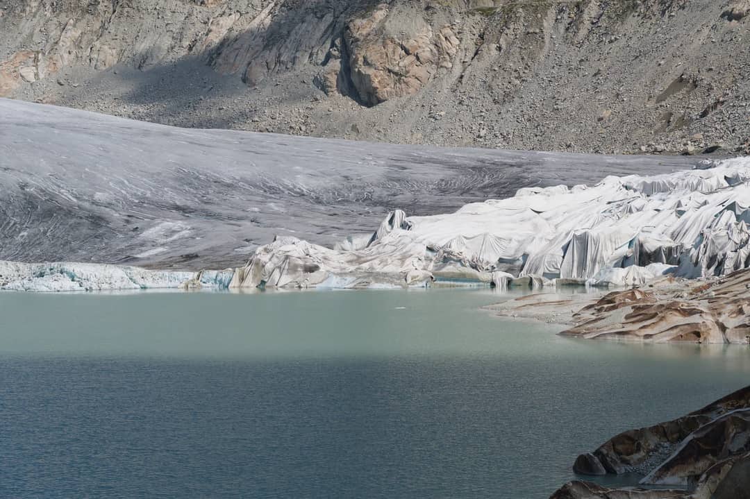 Breathtaking view of a Swiss glacier surrounded by mountains and a serene blue lake, capturing nature's raw beauty.
