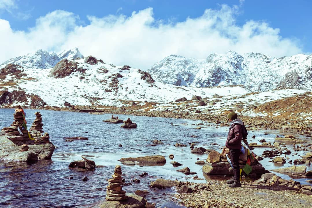 Person standing by a serene snowy lake surrounded by mountains, perfect for adventure and exploration themes.