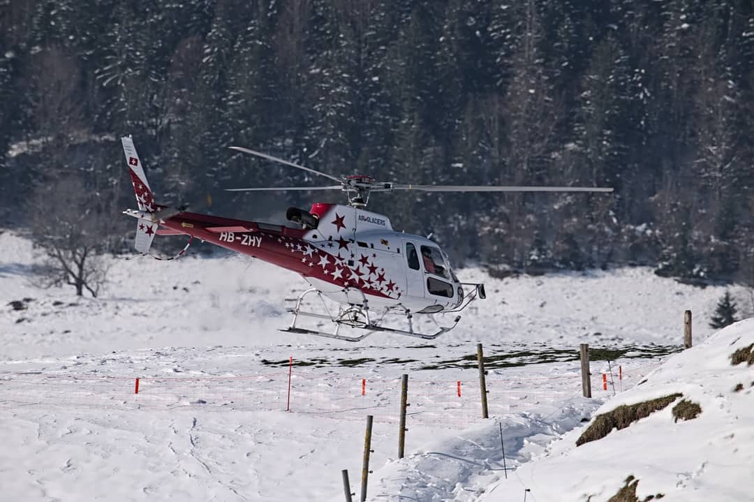 Red and white helicopter in flight over snowy landscape in Château-d’Œx, Switzerland.