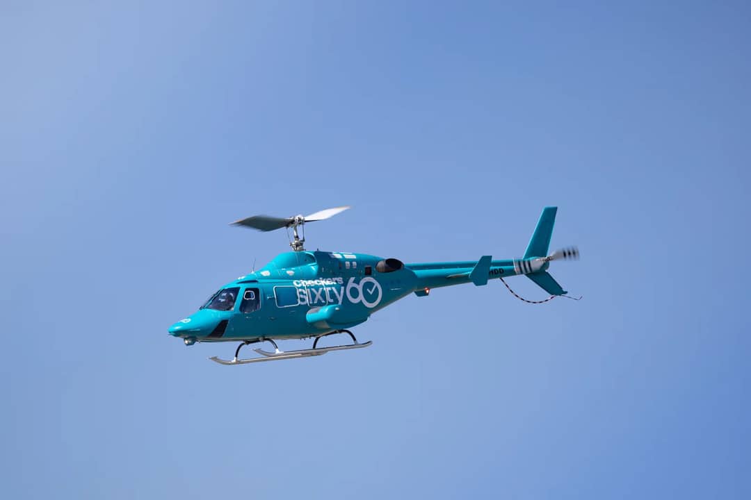 A striking blue helicopter hovering against a backdrop of clear blue skies.