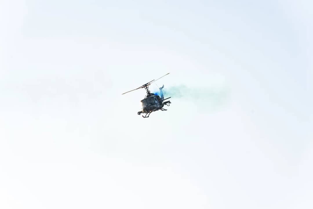 High-altitude helicopter emitting blue smoke in clear El Salvador sky.