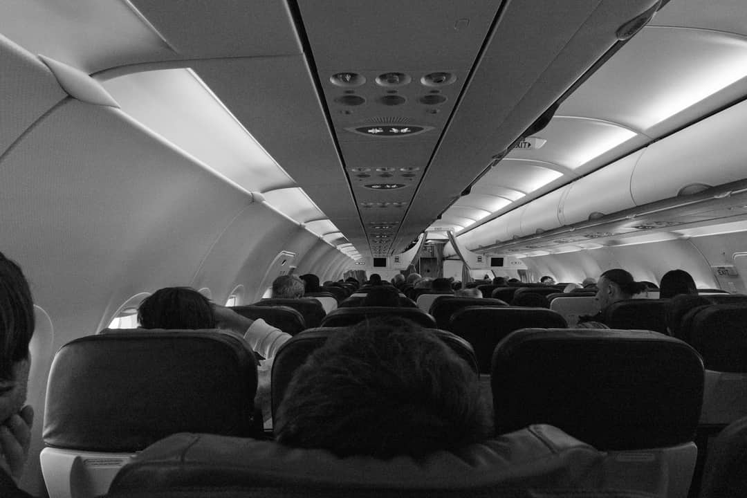 Black and white view of passengers seated inside an airplane cabin.