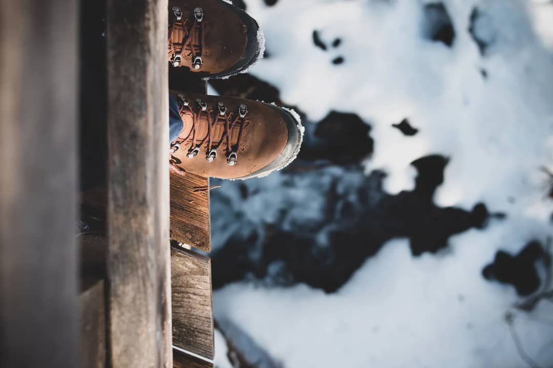 Top view of brown hiking boots on a wooden edge overlooking a snowy landscape, capturing a winter adventure.