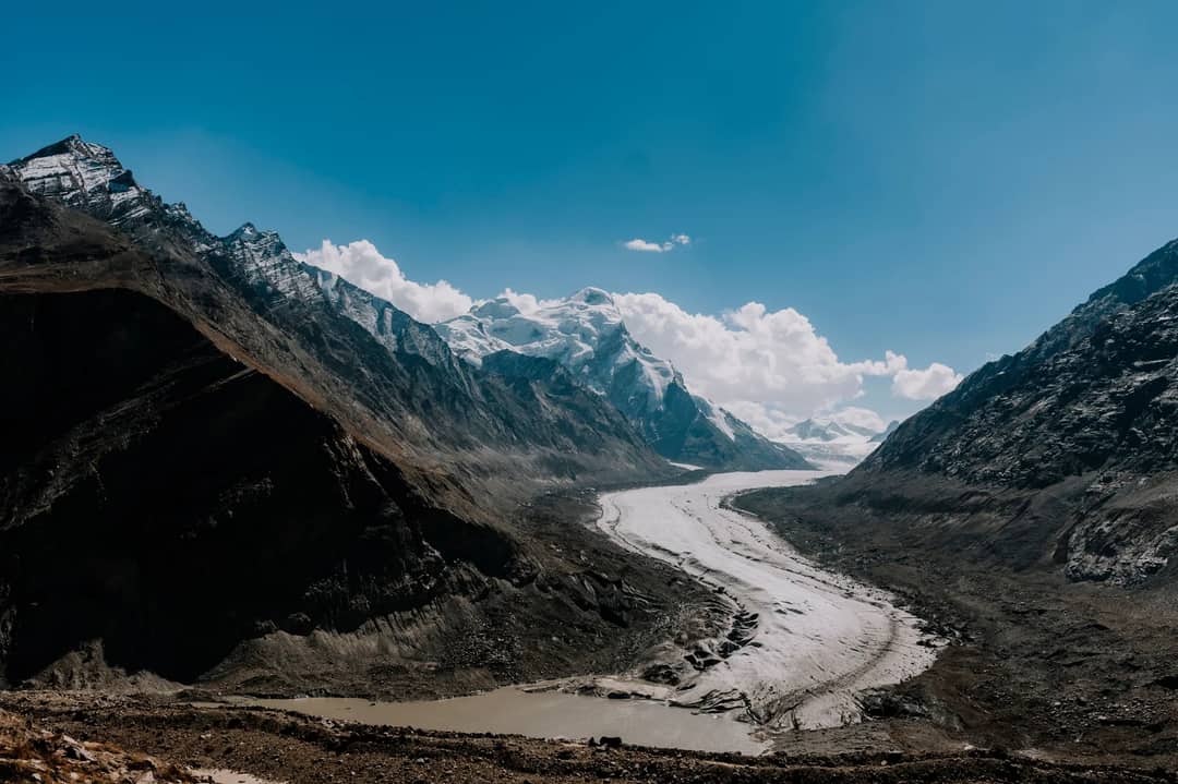 Breathtaking view of a glacier winding through the majestic Himalayan mountains under a clear blue sky.