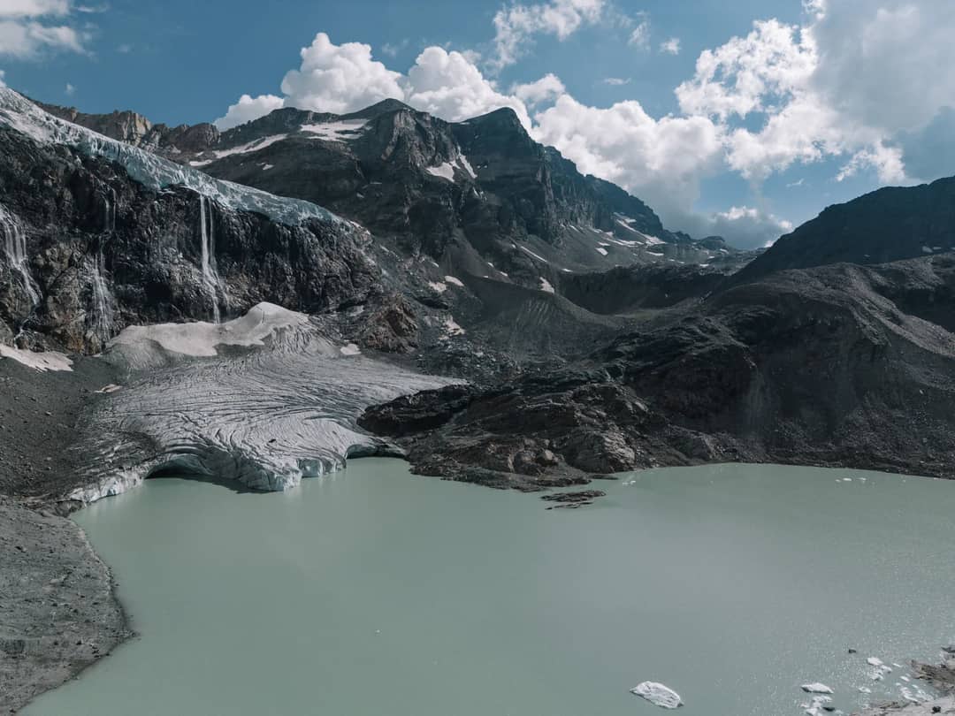 A breathtaking view of a glacier, mountains, and a turquoise lake under a cloudy sky.