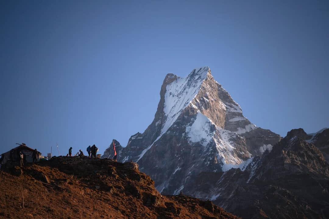 Hikers at Machapuchare base capturing the stunning snowcapped Himalayan peak during daytime.