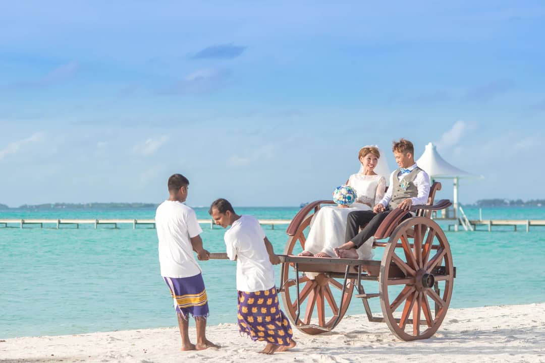 A joyful couple enjoys a cart ride on a scenic tropical beach, perfect for romantic getaway visuals.