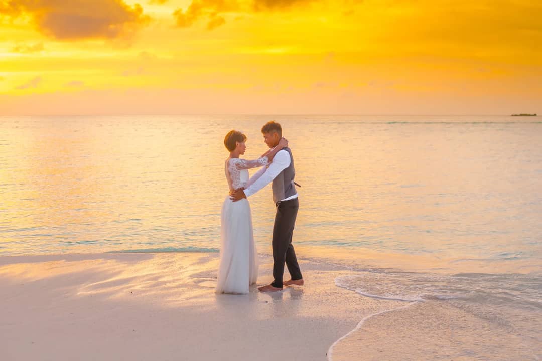 A couple in wedding attire embracing on a golden beach at sunset in Maldives.