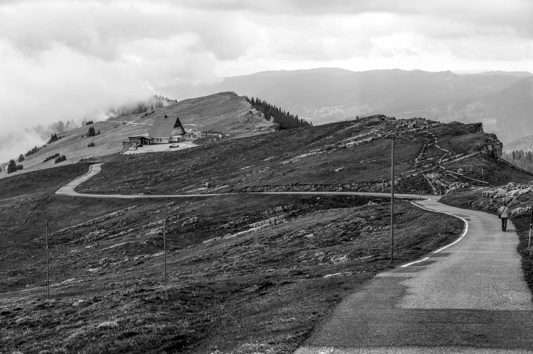 A tranquil mountain scene with a winding road and cabin under a cloudy sky.