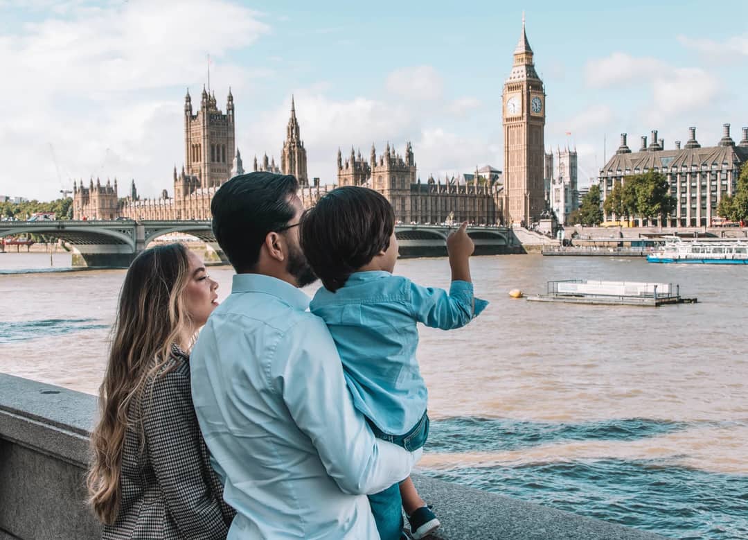 A family admires the iconic Big Ben and Houses of Parliament from a riverside in London, capturing a serene moment.