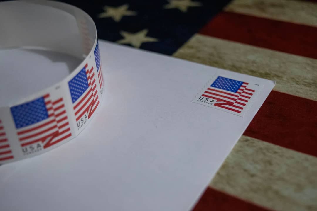 Close-up of USA flag postage stamp on white envelope with American flag background, symbolizing patriotism.