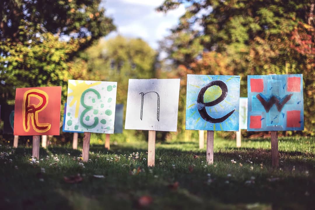 Artistic signs spelling 'Renew' amidst a lush, sunny garden landscape.