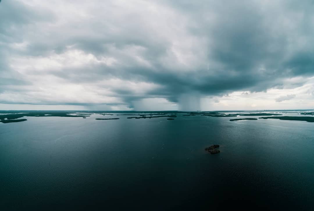 A stunning aerial view of a vast ocean under dramatic cloud formations and rain in the distance.