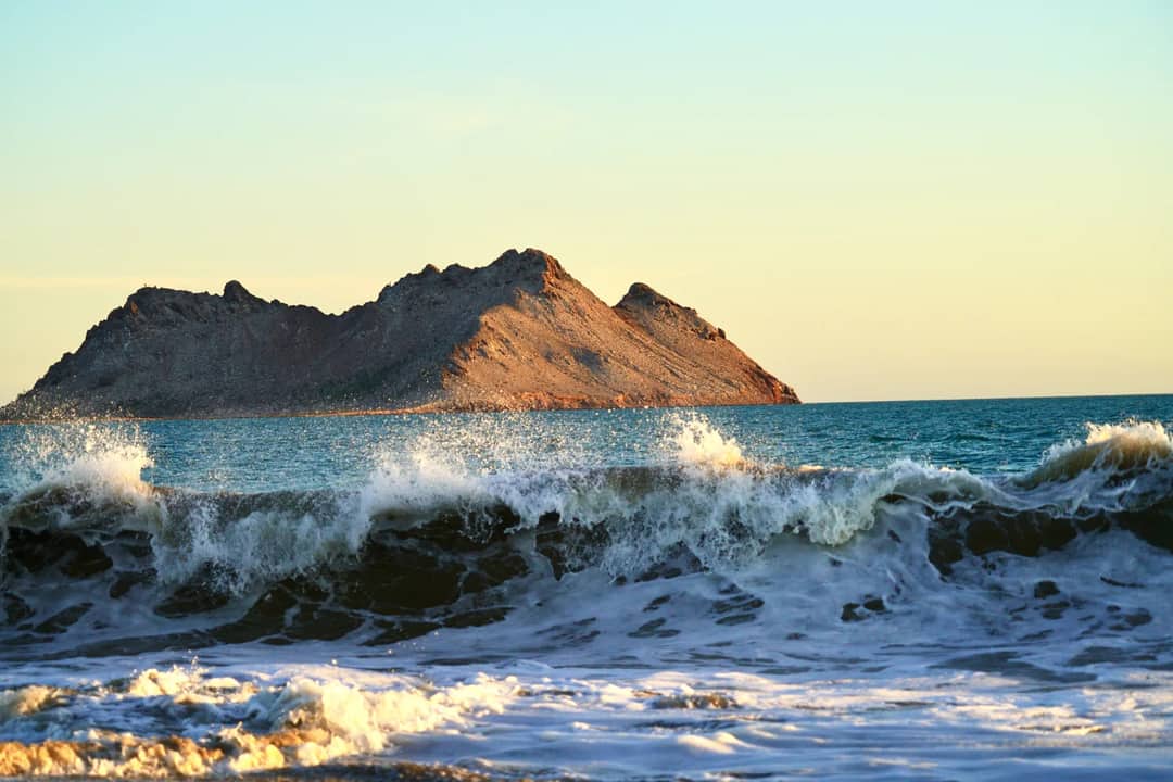 Captivating view of ocean waves crashing against a rocky island in San Carlos, Mexico at sunset.