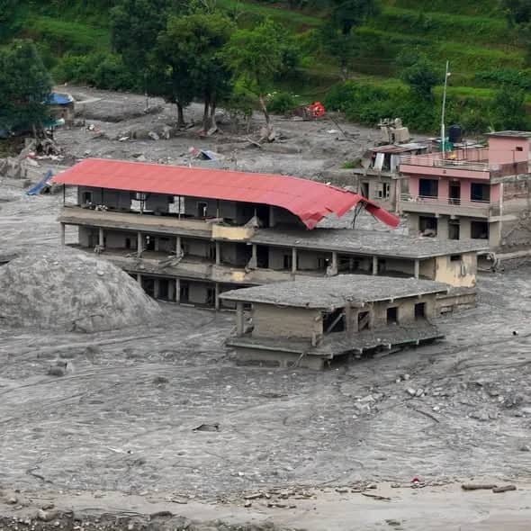 A large multi-storey building with a collapsed red roof, buried to its second floor in flood silt