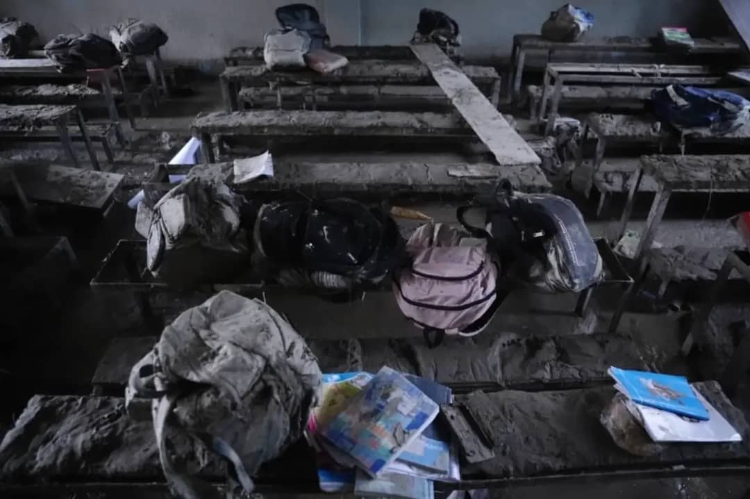 A classroom filled with dried grey silt, school bags and exercise books left on the benches