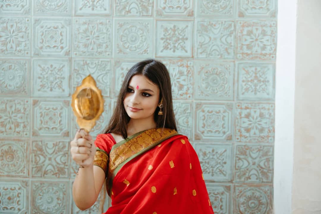 A traditional Indian woman in a red sari holding a hand mirror, showcasing cultural elegance.