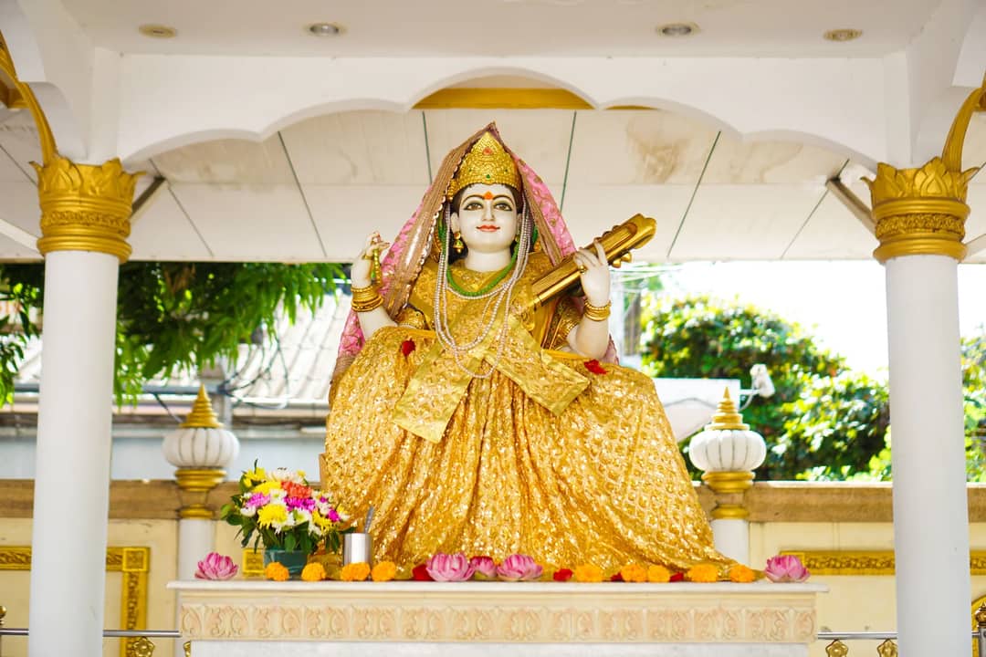 Golden statue of Hindu goddess in an outdoor temple, surrounded by vibrant colors and spiritual offerings.