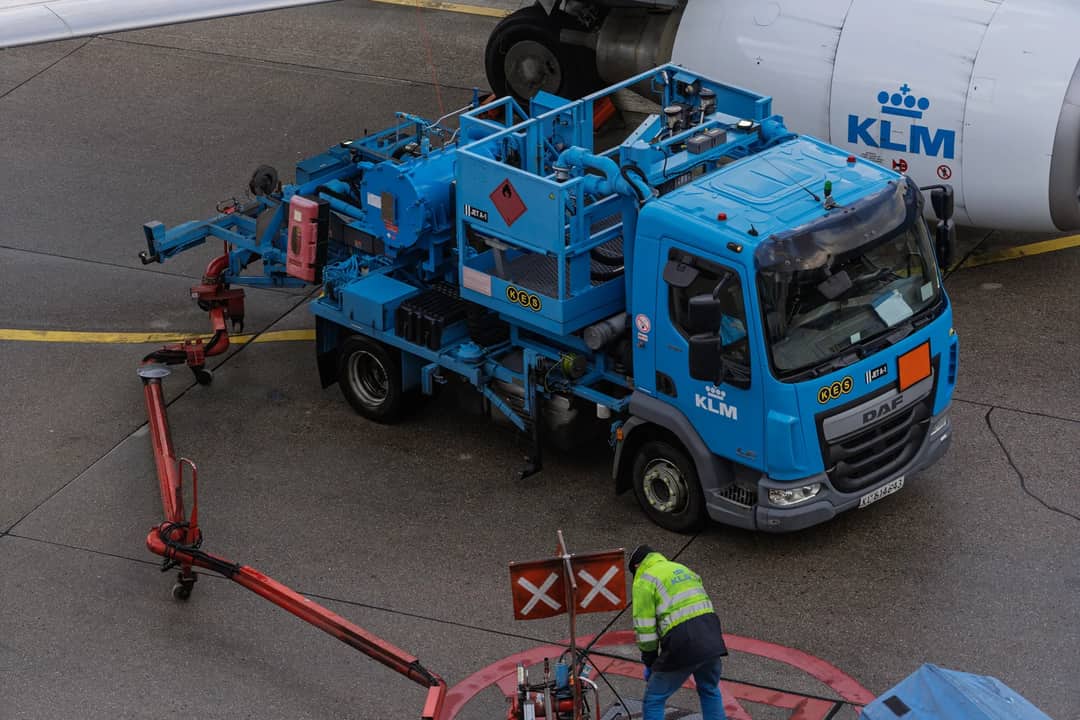 Ground crew at work refueling a KLM airplane with specialized equipment at an airport apron.