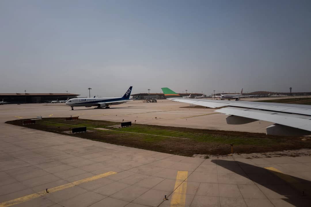 Airplanes taxiing on runway at a busy airport under clear skies.