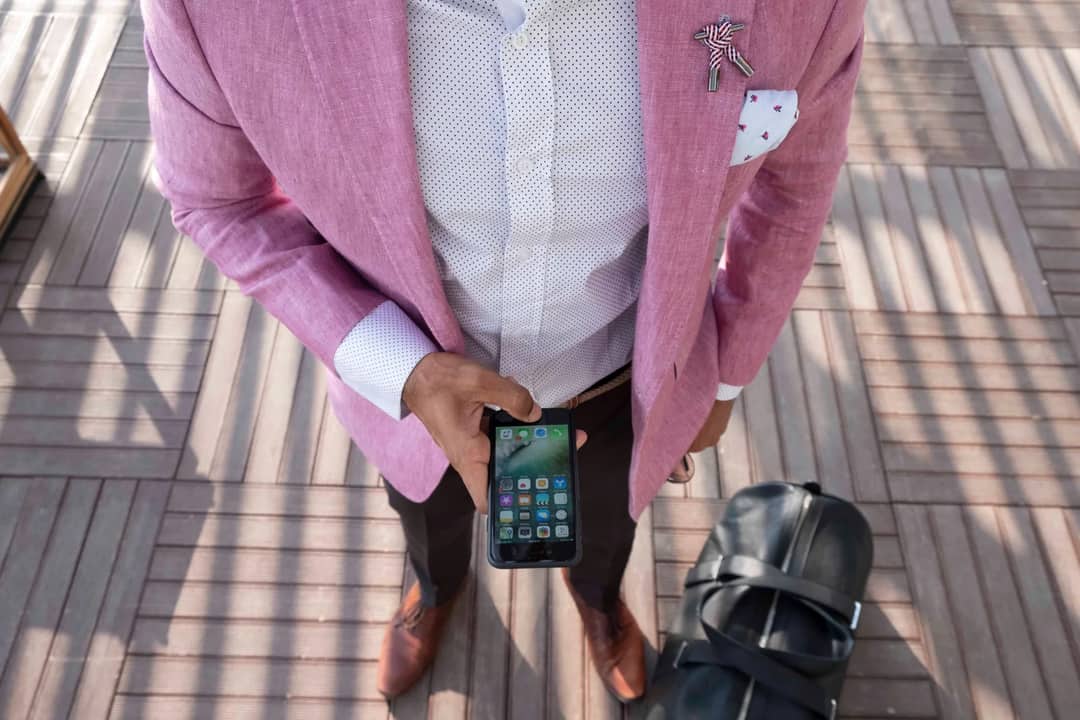 Stylish man in a pink blazer checks his smartphone while traveling with a leather bag.