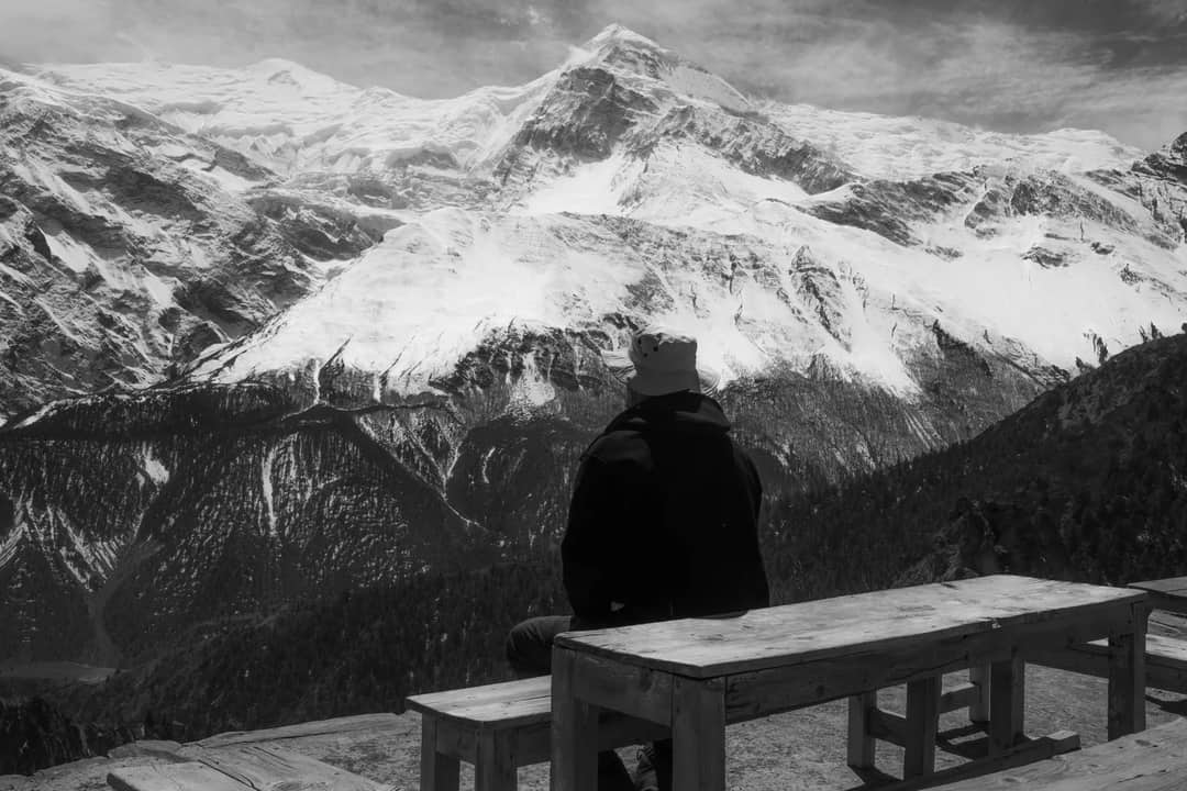 A solitary figure on a bench admires the vast snowcapped mountain range.