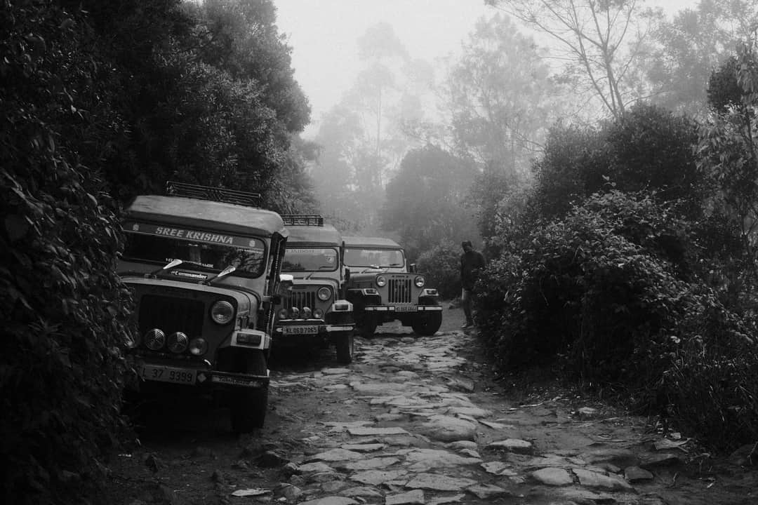 Black and white image of jeeps on a foggy road in Munnar, India, showcasing rugged terrain.