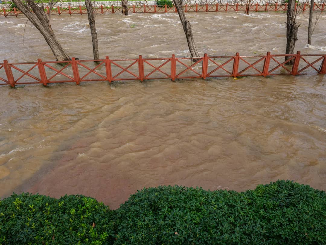 A city park flooded by a swollen river after heavy rainfall, showing the impact of severe weather.