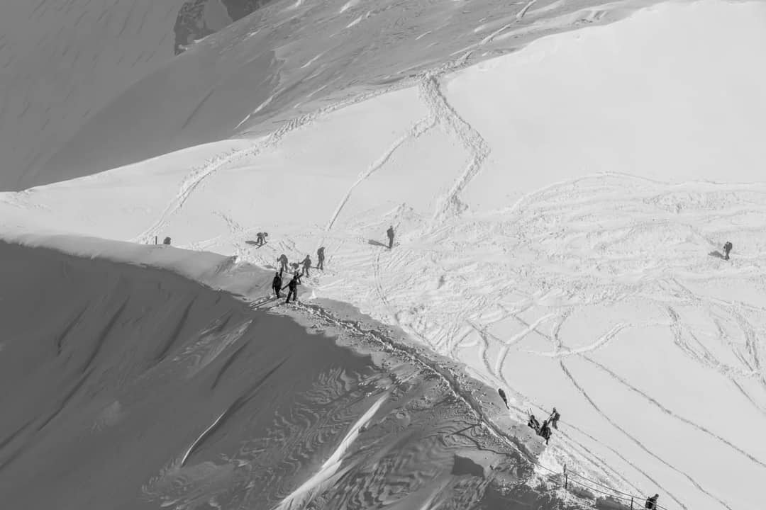 Skiers traverse a snow-covered mountain range in Chamonix, France, under clear skies.
