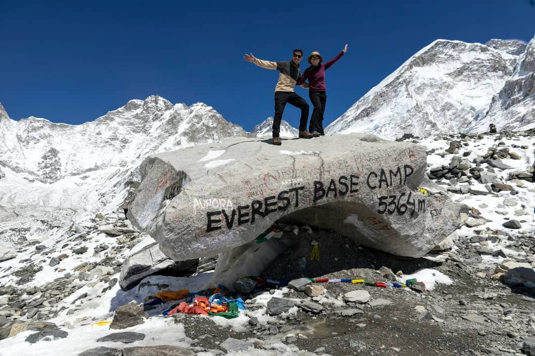 Two people celebrating at everest base camp with mountains behind