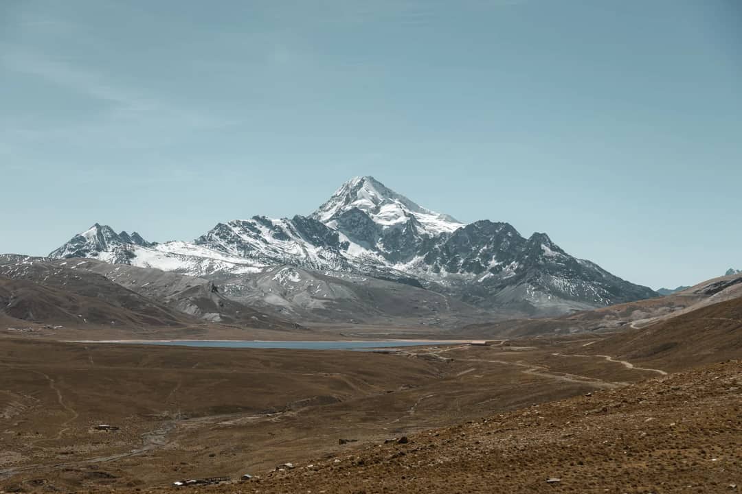 Explore the magnificent snowcapped Huayna Potosi mountain and serene lake in Bolivia's vast landscape.